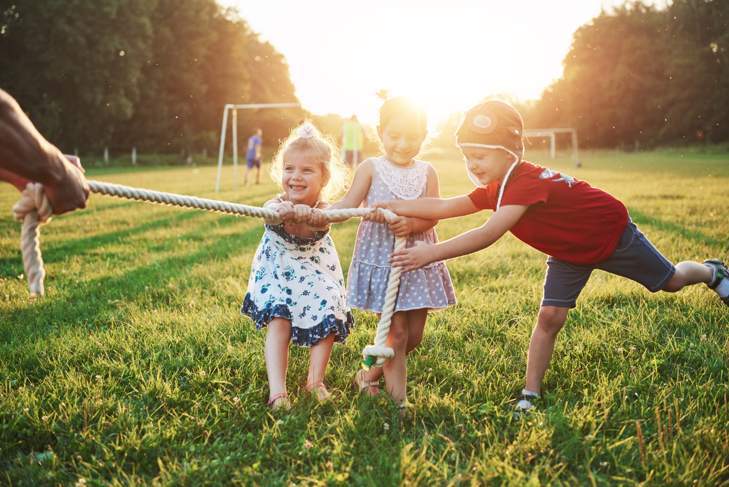 Children play with dad in the park. They pull the rope and have fun laying on a sunny day.