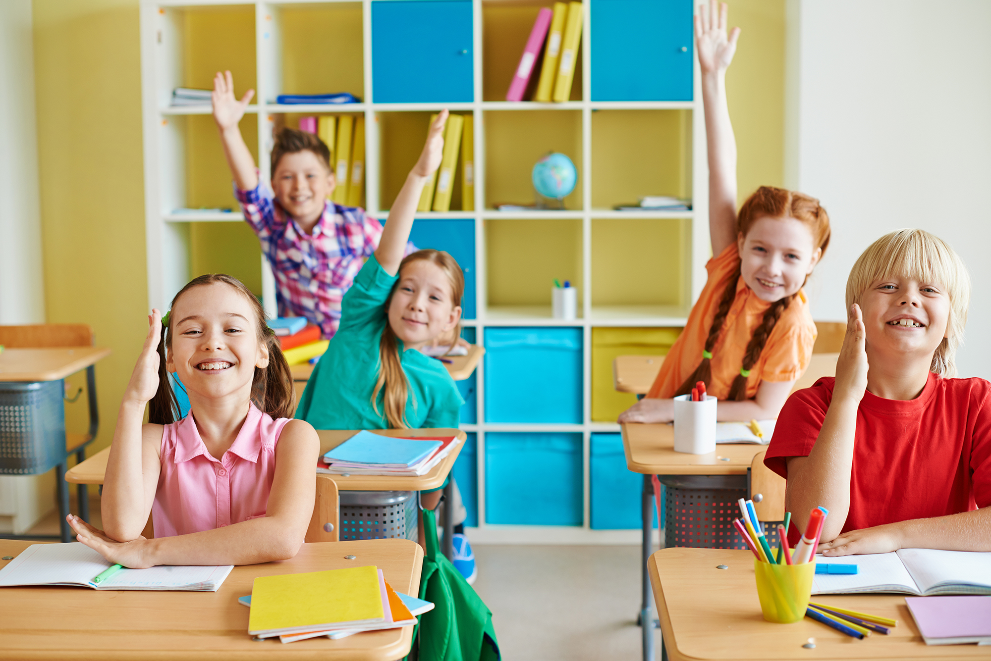 Happy classmates raising hands at lesson